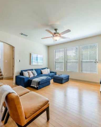 Spacious living room with blue sectional sofa, tan leather chairs, hardwood floors, and large windows with shutters