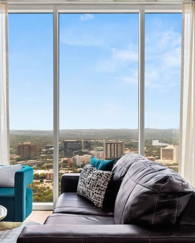 High-rise living room with floor-to-ceiling windows overlooking cityscape, skyline, and river valley with teal and black seating.